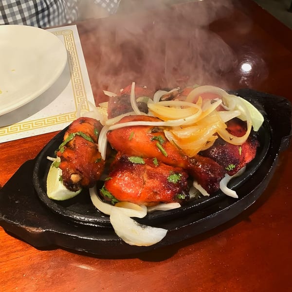 Steaming hot chicken tikka with onions and lime wedges on a sizzling black platter.
