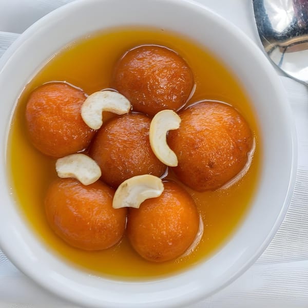 Gulab Jamun, an Indian dessert, in a white bowl with syrup and cashew garnishes.