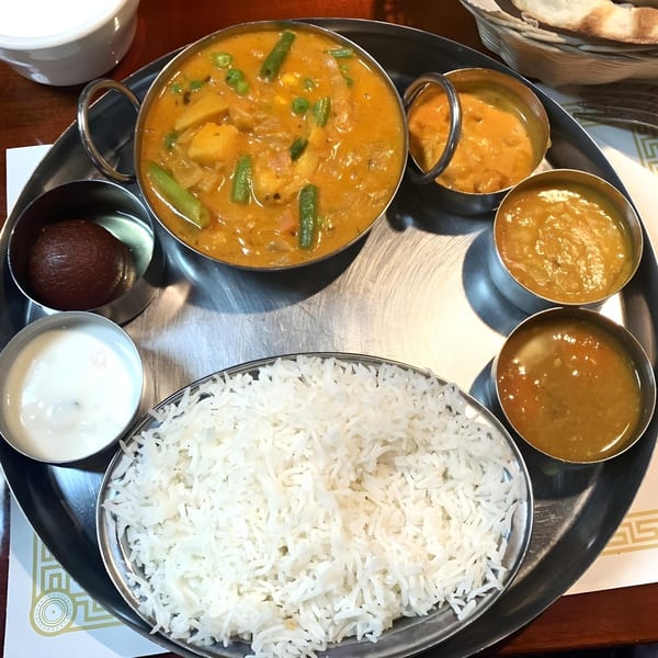 A Masala Indian Cuisine thali with rice, curries, gulab jamun, and yogurt on a metal tray.