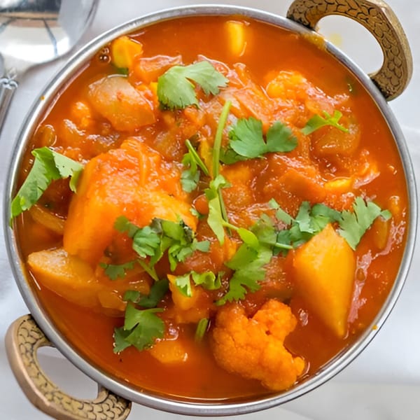 A close-up of a vibrant Indian curry with potatoes, cauliflower, and cilantro in a metal bowl.