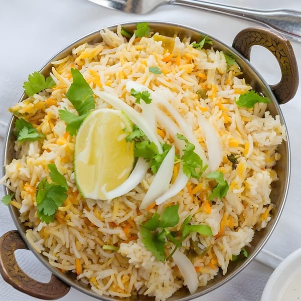 Masala Indian Cuisine's biryani, garnished with cilantro, sliced onions, and a lime wedge in a metal bowl.
