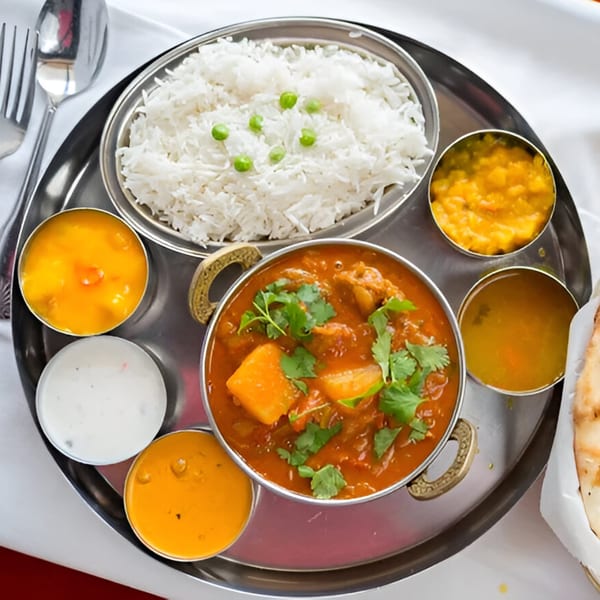 Overhead view of an Indian thali with chicken curry, rice, dal, and chutneys on a silver platter.