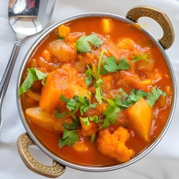 Masala Indian Cuisine's vibrant orange curry with vegetables and fresh cilantro in a metal bowl.